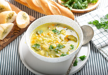 Soup with pickled cucumber and pearl barley in a bowl, on a light background. Pickle in a plate on the table. Rassolnik
