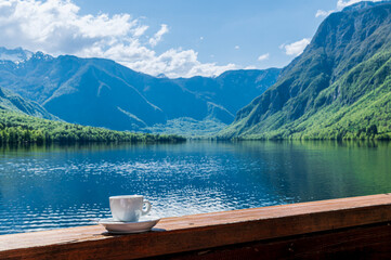 Tasse de café blanche posée sur une rambarde au soleil au bord d'un lac de montagne
