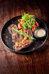A gourmet presentation of grilled steak served on a black plate, accompanied by fresh salad with cherry tomatoes and a creamy dipping sauce, garnished with herbs. Perfect for food photography.