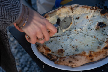 A close up of hands slicing a freshly baked white pizza with a pizza cutter