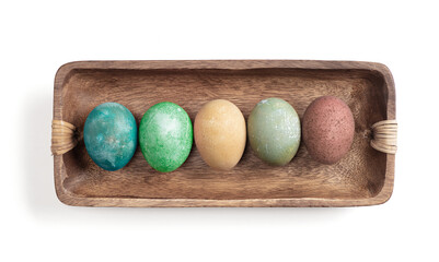 Different easter eggs in wooden bowl on white