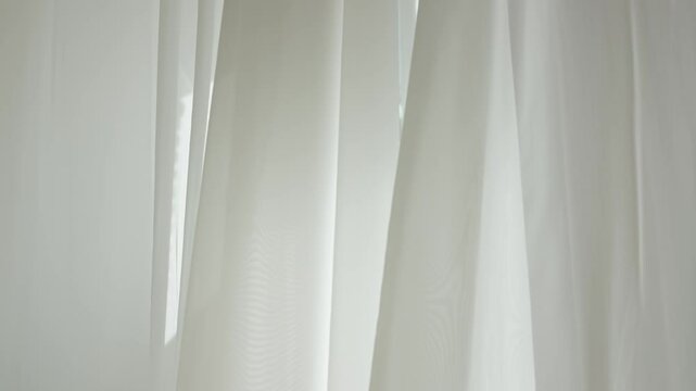 Transparent blurred white silk soft fabrics floating with sunlight shining through, shadows reflected on the textile surface.