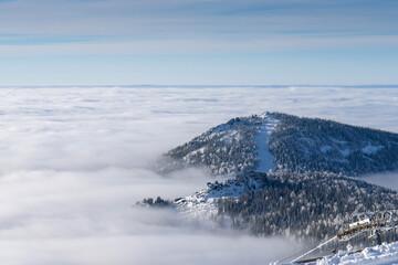 Ski slope on the top of the mountain above the clouds. Aerial winter landscape photo.