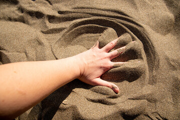 Sandy yellow beach with sea in background, hand touches sand
