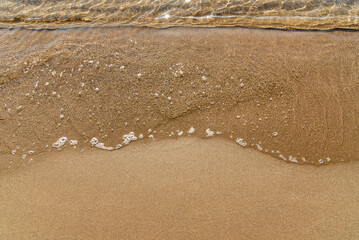 Sandy yellow beach with sea in background, wave ocean in sand