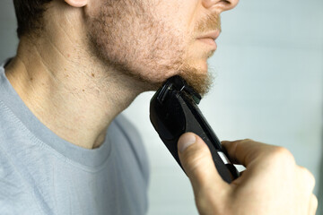 A man trims his beard with a trimmer. Close up. An electric razor trimming a beard. Beard care at...