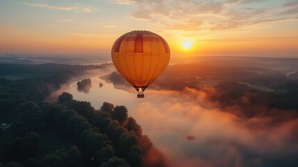 Obraz premium A vibrant hot air balloon floats above a misty river at sunrise, creating a serene landscape.