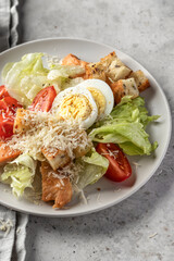 Caesar salad with chicken meat, green iceberg salad, eggs, tomatoes and parmesan cheese on gray background close up