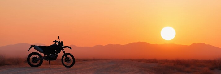 A motorcycle is parked in the desert at sunset. The sky is orange and the sun is setting