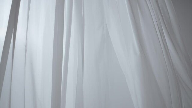 Transparent white silk soft fabrics floating with light shining through, shades shadows of window silhouette reflected on the textile.