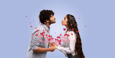 Indian couple stands facing each other, sharing an affectionate kiss. Surrounded by floating hearts, they hold hands in a moment of love and connection during a special celebration.