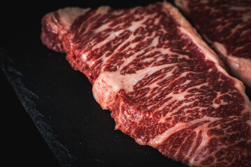Raw marbled beef steaks on a black mica board and a dark background. Place for text. Close-up