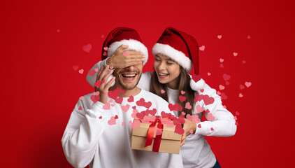A couple joyfully shares a moment while celebrating Valentine's Day, with playful gestures and a surprise gift. They express their affection in a lively, festive atmosphere filled with hearts.
