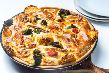 Quiche in a baking dish on a wooden board on a white table. Open pie with cheese, chicken, broccoli and corn with a golden crust. Traditional French quiche