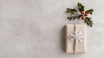 Fototapeta premium A minimalist Christmas flatlay featuring a small, wrapped gift in soft kraft paper, a sprig of holly, and a snowflake ornament, all arranged neatly on a pale gray surface with natu