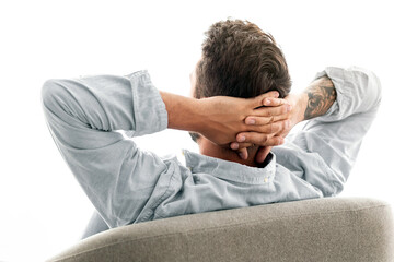Obraz premium Weekend leisure. Happy young man sitting in armchair, relaxing and holding hands behind head, looking at window and enjoying silence. Millennial guy sitting back to camera