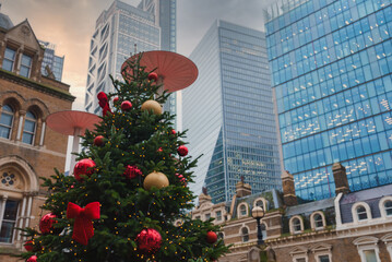 A large Christmas tree with red and gold ornaments stands amid London's modern skyscrapers,...