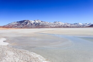 Snow-capped mountains and frozen salt flat in Atacama Desert.