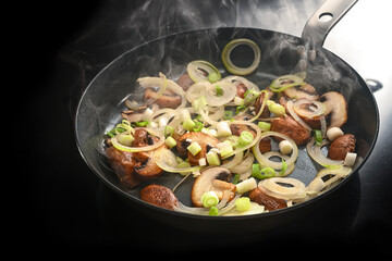 Mushrooms and onions are fried in a steaming frying pan on a black induction hob, homemade cooking a tasty meal, copy space, selected focus