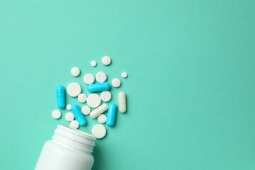 Various pills pouring out of medicine bottle on color background
