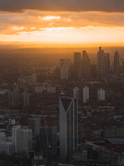Fototapeta premium The image shows London's skyline during sunset, featuring silhouetted skyscrapers against a vibrant orange and gold sky, highlighting urban architecture.
