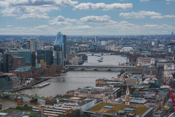 Obraz premium The image captures London's urban landscape with the River Thames, the Shard, and the London Eye. Modern and historic architecture blend under a cloudy sky.