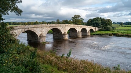 Fototapeta premium Stone arch bridge with multiple arches, crossing a wide river in the countryside
