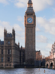 Obraz premium Big Ben clock tower stands tall against a partly cloudy sky, with the River Thames in the foreground. Gothic architecture is highlighted by soft lighting.