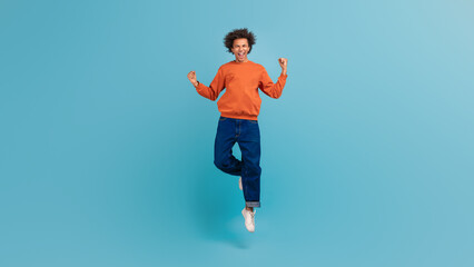 A young African American man with curly hair celebrates by jumping in the air, showcasing a lively...