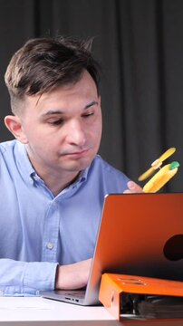 vertical video man works on a laptop in the office and blows with a hand fan