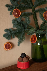 Green fir branches with dried orange slices in glass vase and red ceramic dish with chocolate...