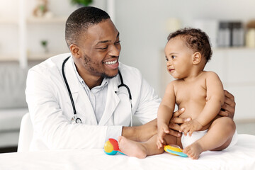 Child's Healthcare Concept. Portrait Of Smiling Black Doctor Making Check Up For Little Infant Baby...