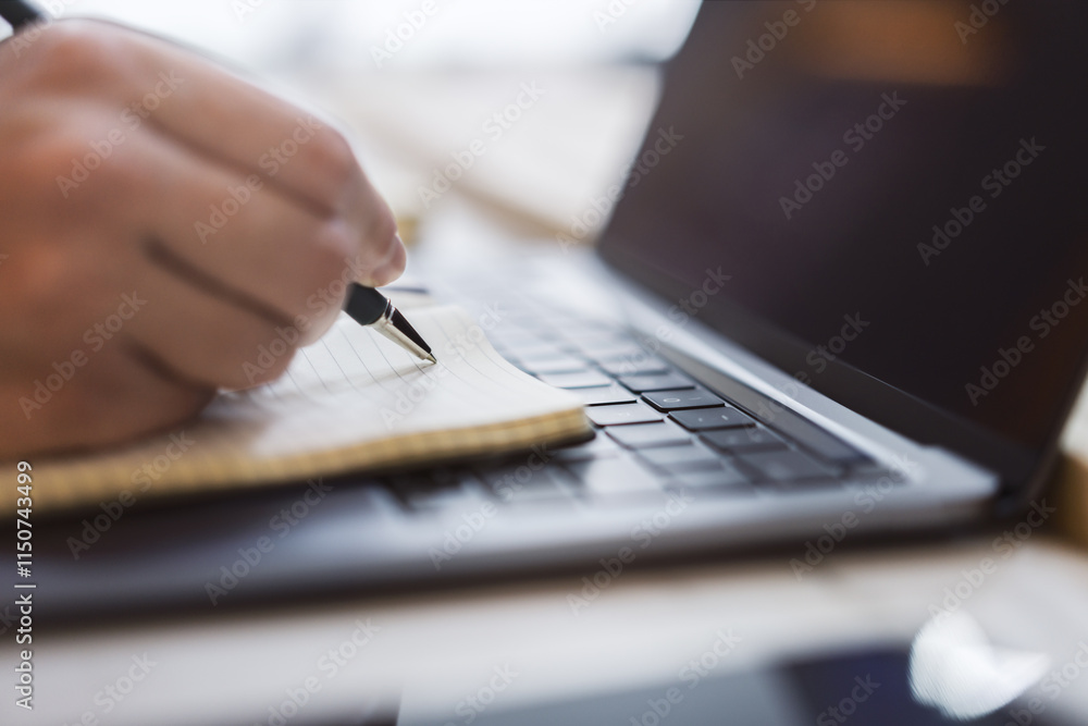 Poster sharp view of a woman's hand transcribing in a notepad on a cutting-edge laptop, with a defocused ba