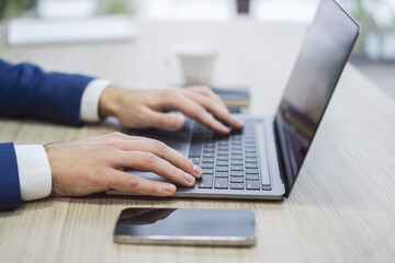 Set against a blurry office setting, a close-up reveals a man's hands typing on a sleek laptop keyboard