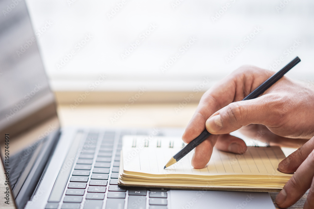Poster the image highlights a man's hand writing in a notepad on a laptop, with a faintly blurred surroundi