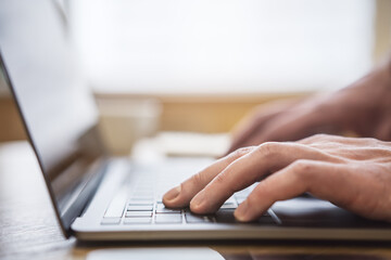 Set against a blurry office backdrop, the image captures a man's hands in close detail, typing on a cutting-edge laptop keyboard