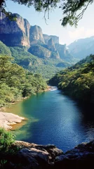 Fototapete Lush river surrounded by mountains in a vibrant green landscape during daylight hours © olegganko