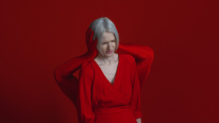 Fototapeta premium External and internal condemnation. Public opinion closes my ears to my needs. A feminist concept. Mysterious red hands surround and cover the ears of a woman in red, a photo on a red background.