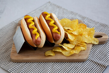 Homemade Boiled Hot Dogs with Mustard and Potato Chips on a Wooden Board, side view.