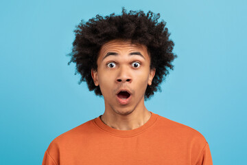 A young African American man with curly hair shows a look of surprise against a vibrant blue background. His expression conveys a strong emotion, highlighting a moment of realization or shock.