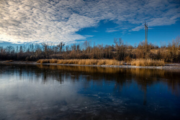 Winter landscape on the pond,frozen pond,blue colors .Landscape with water and ground.Reed on the beach , frozen lake at the morning with sunlights on the sky.Beautiful clouds in the sky,cold and snow
