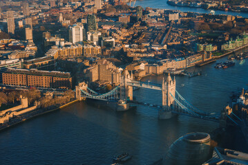 An aerial view of London's Tower Bridge over the River Thames at sunset. The City Hall's curved...