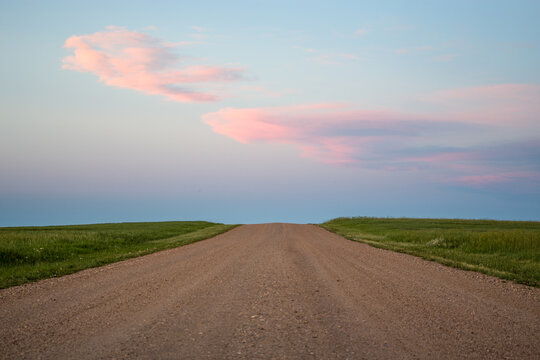 pastel clouds in the sky with dirt road leading to it rolling hills grass lands in badlands national park during sunset 