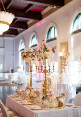 Guest table in a restaurant decorated with gold candlesticks and flowers. Beautiful decoration of a dining table in a restaurant at a wedding banquet. Preparation for a banquet in a restaurant