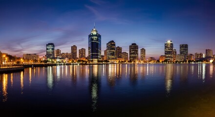 Fototapeta premium A panoramic view of a city skyline at dusk with glowing lights reflecting on the water