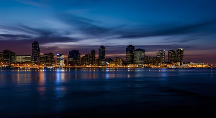 Fototapeta premium A panoramic view of a city skyline at dusk with glowing lights reflecting on the water