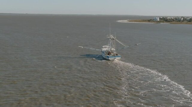 Low aerial shot following a commercial shrimping vessel as it pulls nets off the coast of South Carolina.