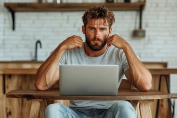 A bearded man appears focused while seated at a wooden table, working on his laptop. The rustic kitchen background complements his relaxed, thoughtful demeanor.