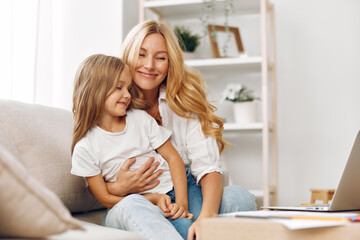 Mother and daughter bonding over a laptop on a cozy couch, engaging in educational or entertaining activities together