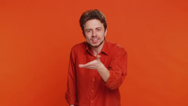 I cant hear you. What. Caucasian man trying hear you looking confused and frowning keeping arm near ear for louder voice asking to repeat, to hear information, deafness. Young guy on orange background